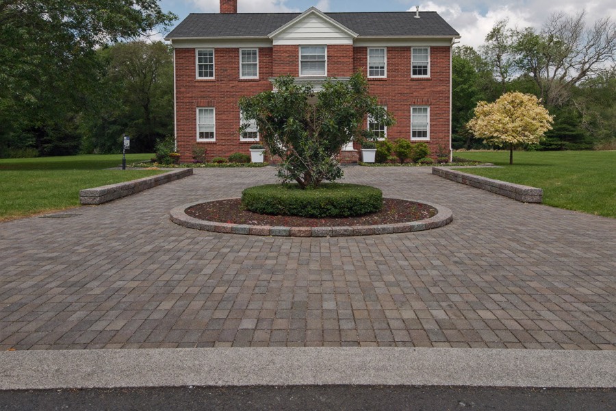 A circular paver drive around a round planted island in front of a red brick house.