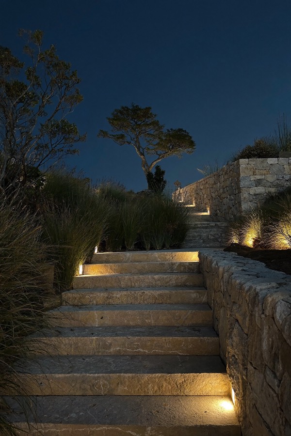 Wide stone garden steps at night with warm lights set into the risers beside a stacked-stone wall.