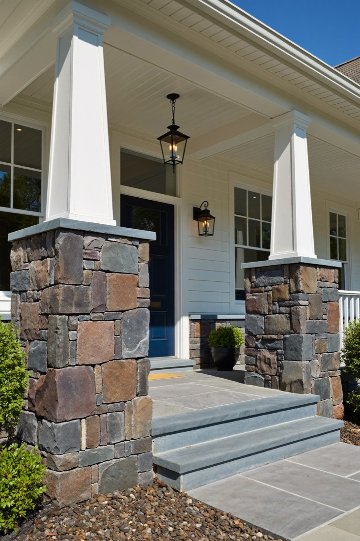 Front porch piers clad in mixed grey and brown stone, beside wide blue-grey stone steps leading to a navy front door.